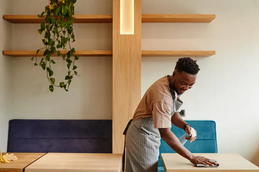 A smiling Bedeen Cleaning Services team member wiping down a table